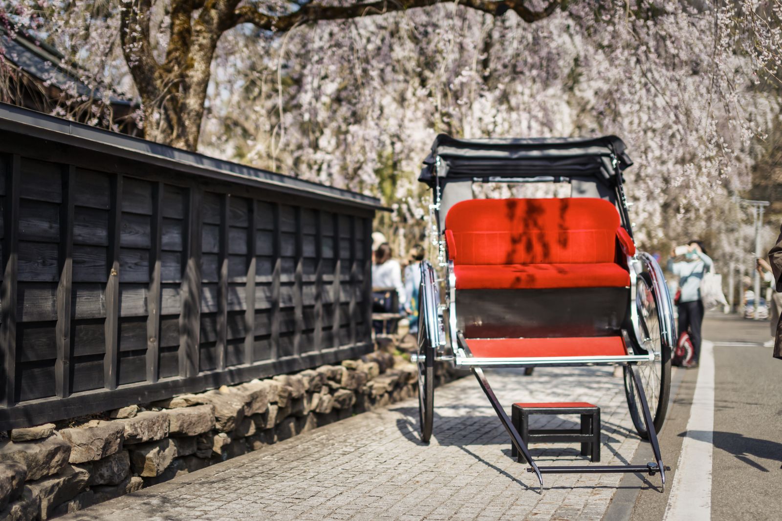 Rickshaw waiting beside black samurai-house walls under weeping cherry at Kakunodate