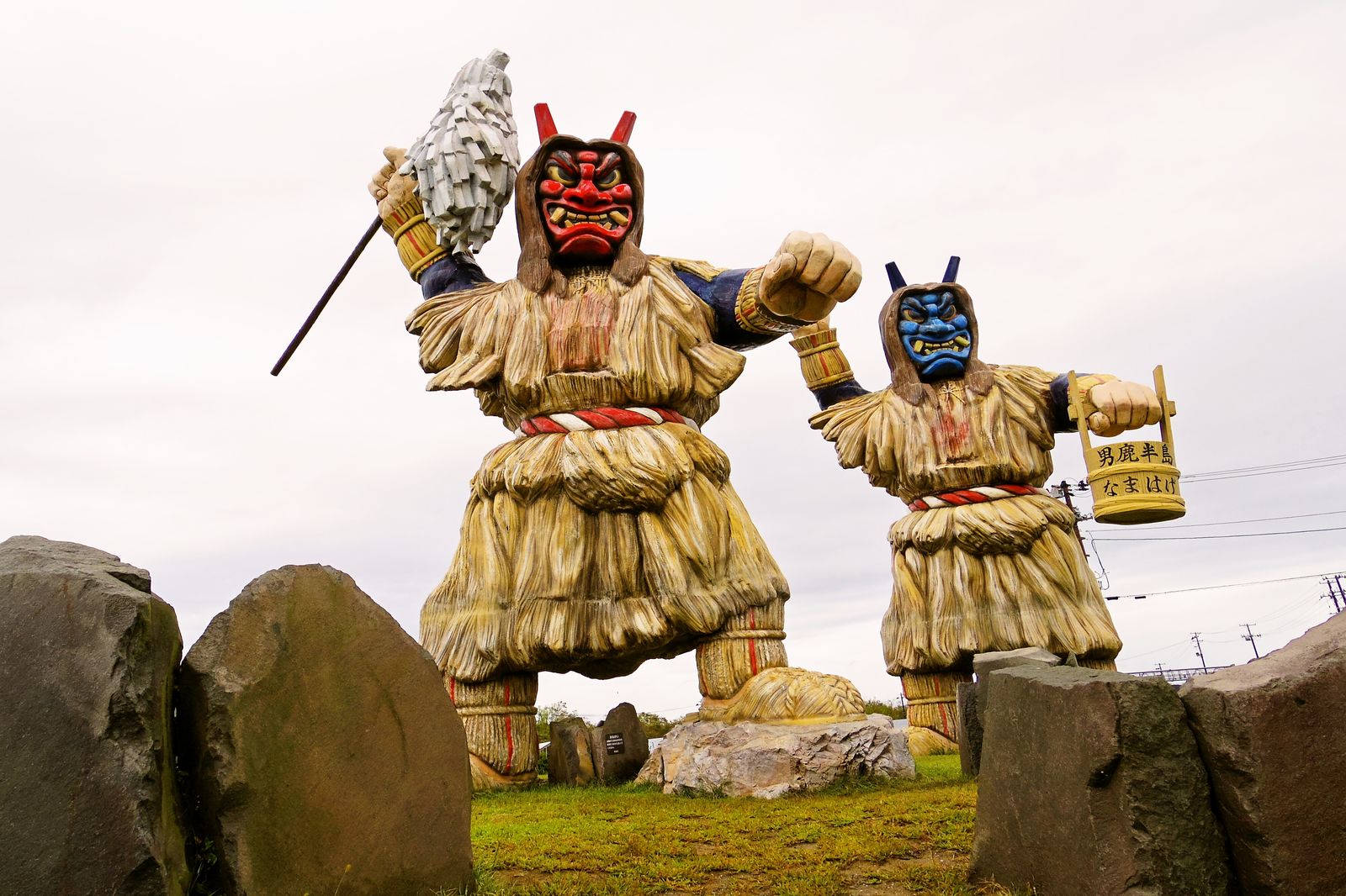 Two towering Namahage figures in straw capes with red and blue demon masks at the Oga peninsula