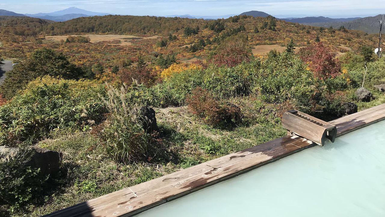 Open-air hot spring bath at Sukawa Onsen looking across autumn hillsides to distant peaks