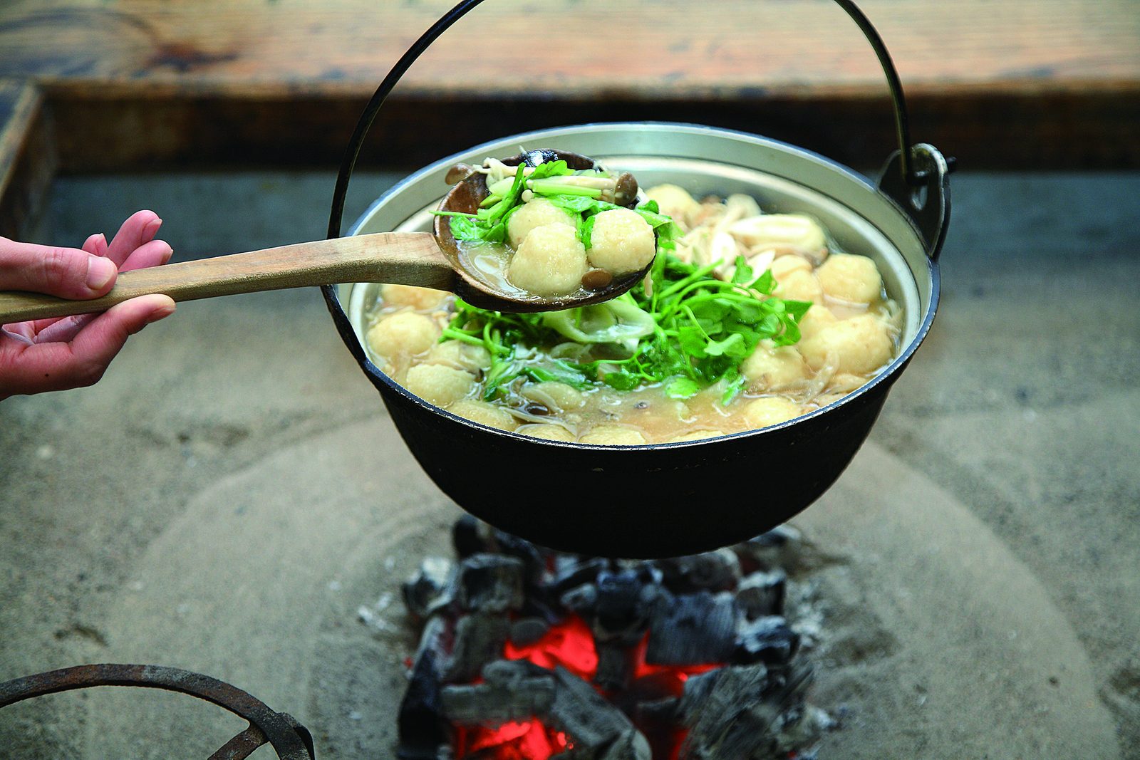 Yamano-imonabe hot pot simmering in a cast-iron pot over charcoal, with dumplings and greens