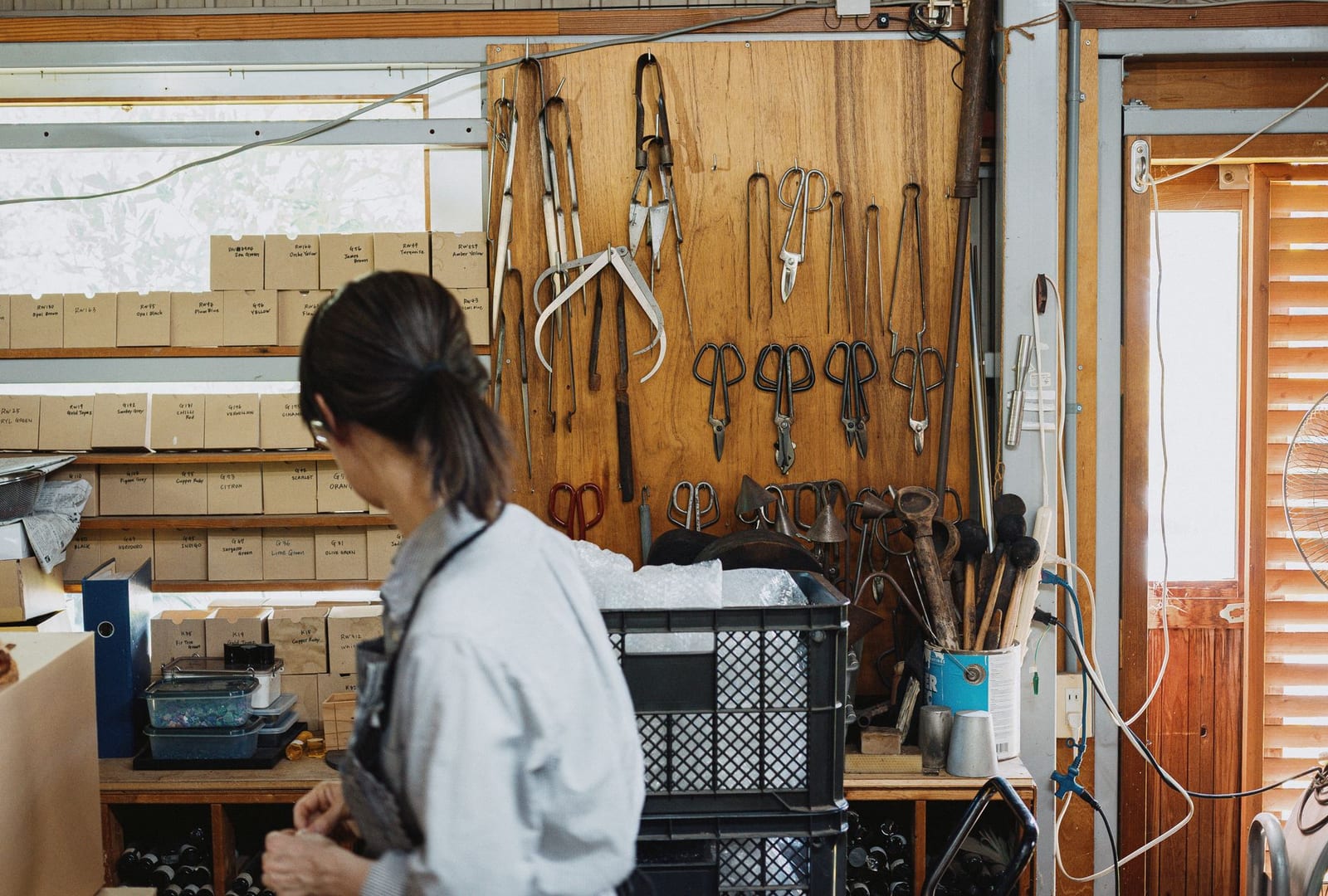 An artisan at work at a bench in a traditional Japanese workshop hung with hand tools