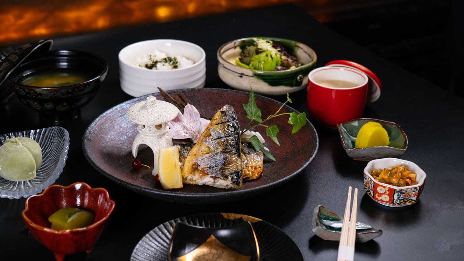 Seasonal multi-course Japanese meal plated across ceramic dishes and lacquer bowls