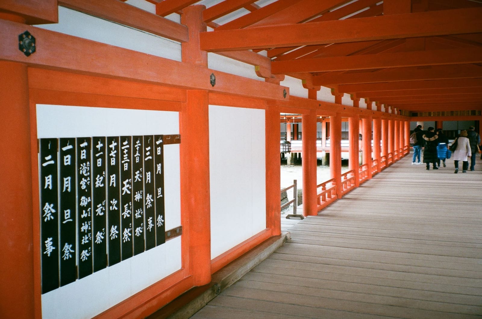 Vermilion corridor of Itsukushima Shrine with visitors walking through