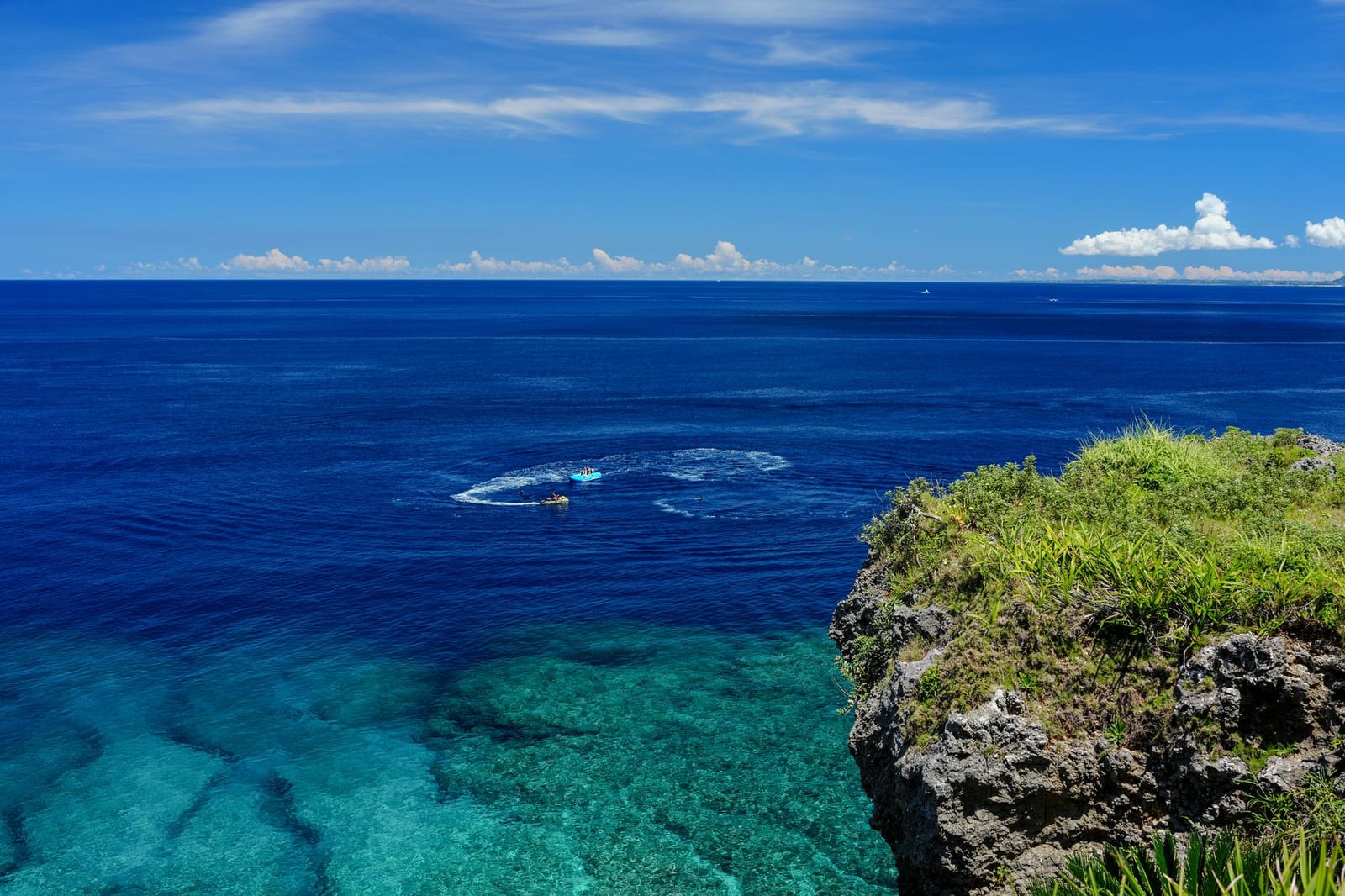 Clear turquoise sea below a green headland on the Okinawa coast