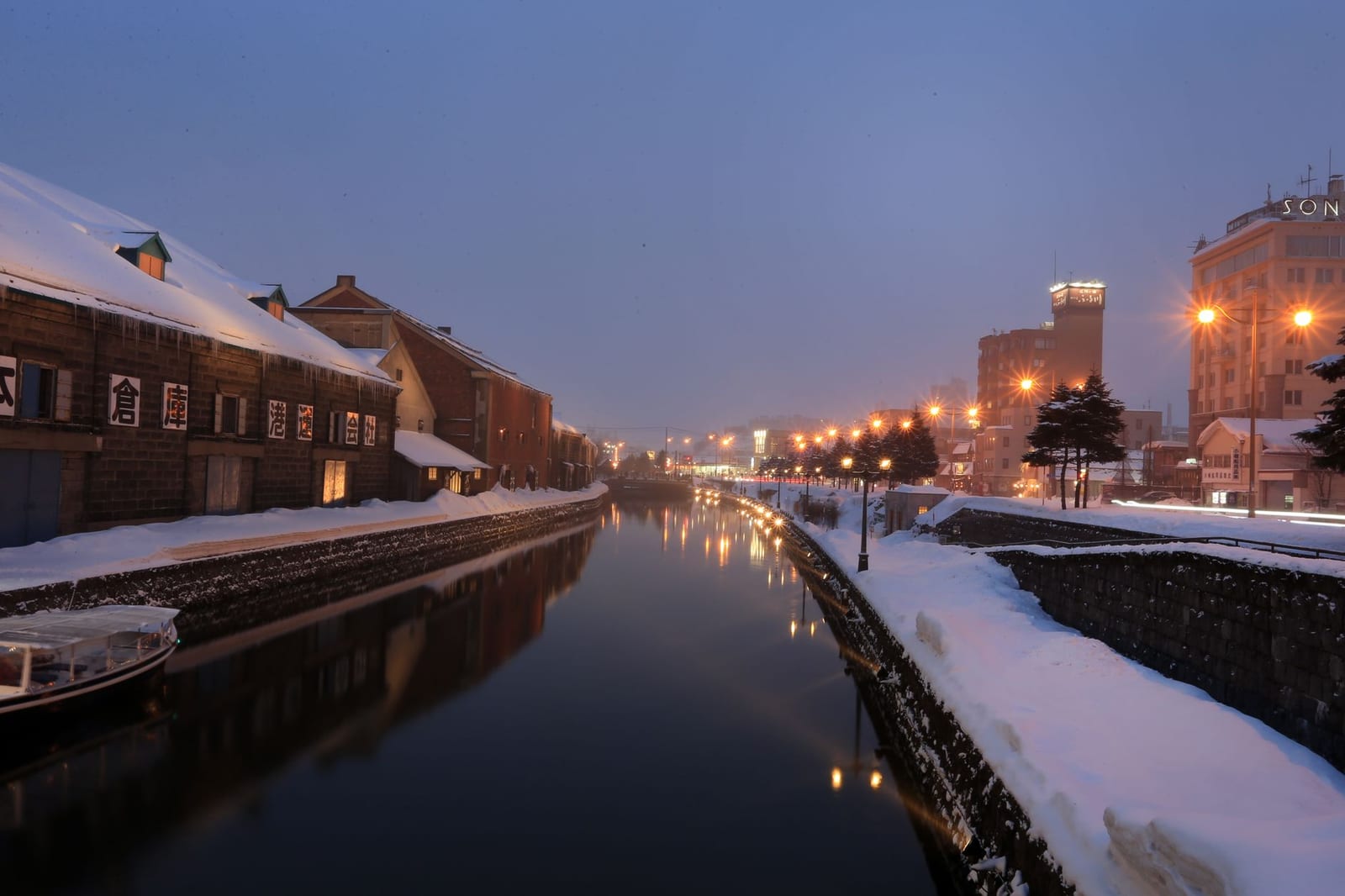 Otaru canal at dusk in winter, with warehouses and lit lamps reflected in the water