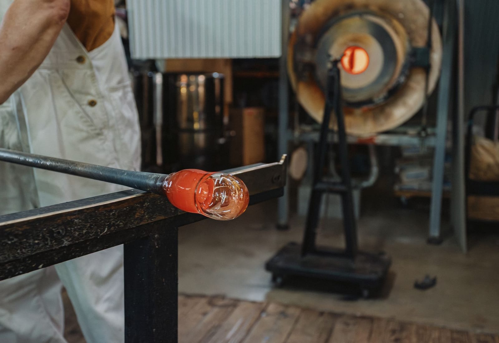 Glassblower shaping molten glass at a workshop bench