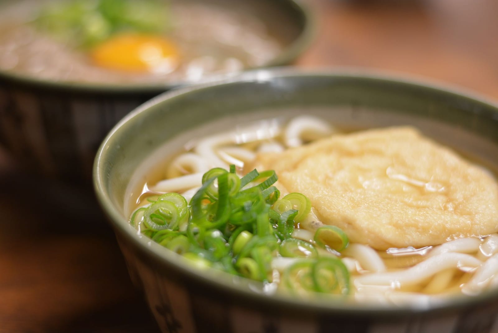 Bowl of thick udon noodles in broth topped with spring onion and tofu