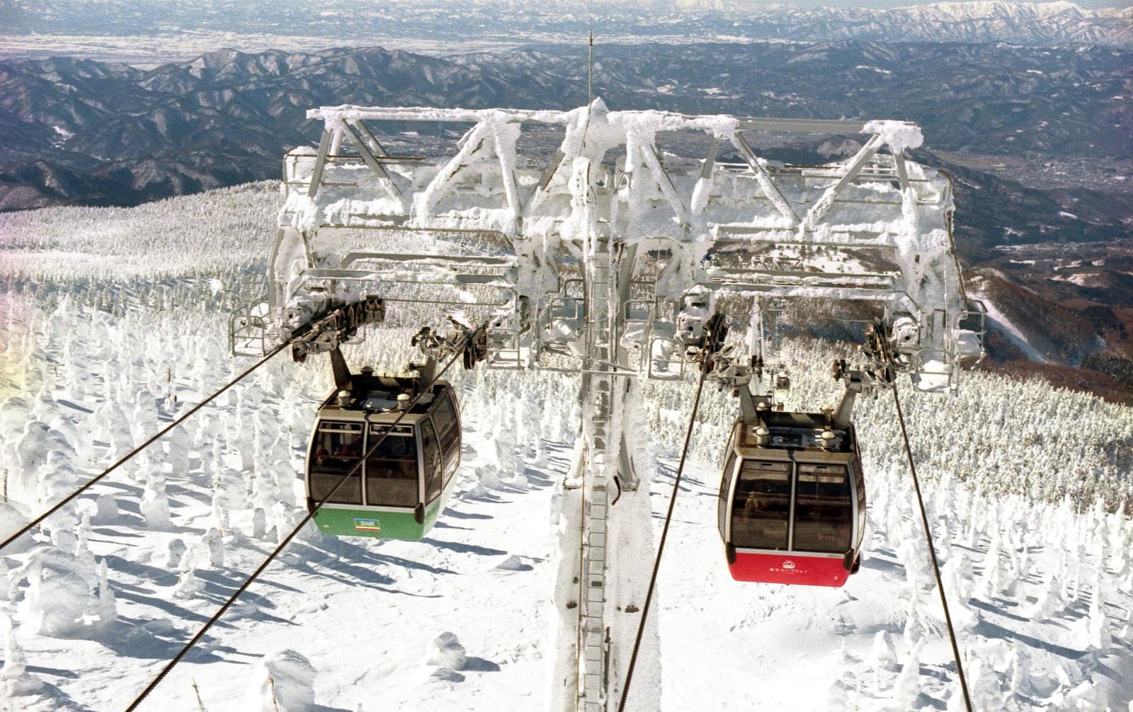 Gondolas passing above frost-covered trees on a mountainside in Yamagata